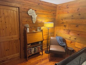 A cozy room with wooden walls, a bookshelf, a chair, and a floor lamp.