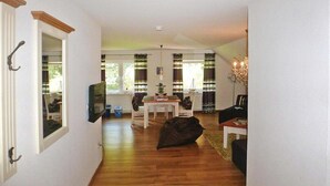 Un couloir mène à une salle à manger où se trouvent une table et des chaises, un fauteuil poire et un lustre.