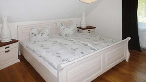 Un lit blanc avec une literie à motifs floraux, une table de chevet avec un vase et un luminaire suspendu.