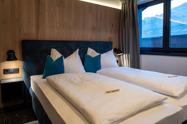 Una cama doble con almohadas blancas y azules, un cabecero de madera y una mesita de noche con lámpara.