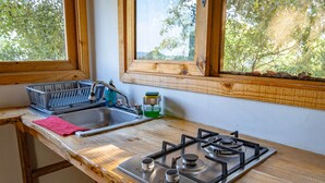 A kitchen with a gas stove, a sink, a window with a view of trees, and a wooden countertop.