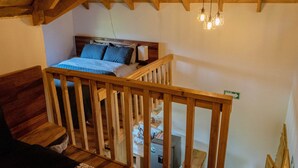 A bedroom with a wooden headboard, a bed with blue bedding, a wooden railing, and a ceiling light fixture.