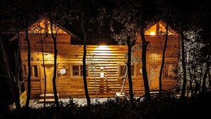 A wooden cabin with a central entrance and two side entrances, surrounded by trees.