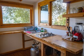 Une cuisine dotée de plans de travail en bois, d’une cuisinière à gaz, d’un évier et d’une fenêtre donnant sur un espace verdoyant.