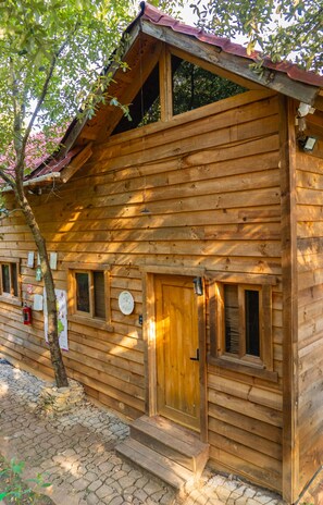 Une cabane en bois avec un toit rouge, une porte en bois et une fenêtre dotée d’un volet.
