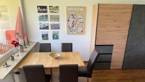 En matplats med ett träbord, svarta stolar och en anslagstavla med resebilder och en skylt med texten ”DUBUFT”.