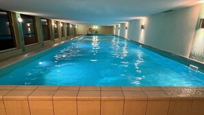 En inomhuspool med kaklade väggar och ett kaklat golv, omgiven av fönster och lampor.