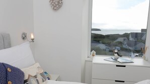 Ein Schlafzimmer mit Bett, Nachttisch mit Lampe, Meerblick und einer kleinen Dekoration auf der Fensterbank.