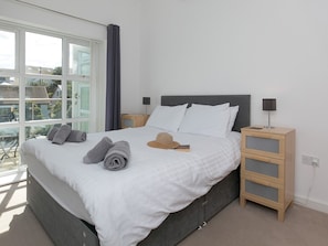 Quarto moderno com cama grande, mesa de cabeceira de madeira e vista para o exterior.