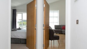 A room with a bed, a grey sofa, and a wooden door. - 2 Bed Sea View Apartment with Balcony Parking - Pass the Keys (Benllech)