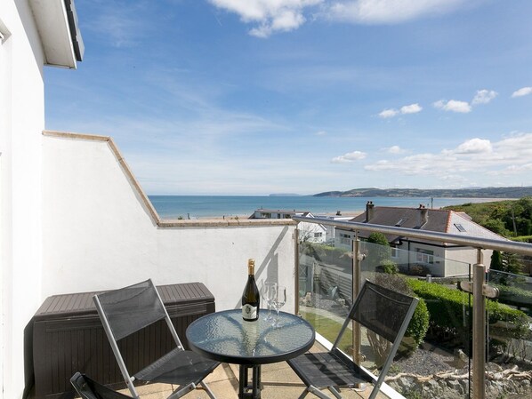Uma varanda com mesa e cadeiras de vidro, com vista para a praia e o mar.