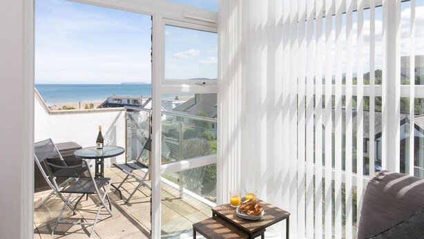 A balcony with a view of the sea, a table with glasses and a bottle, and a chair. - 2 Bed Sea View Apartment with Balcony Parking - Pass the Keys (Benllech)