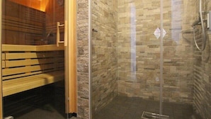 Un baño moderno con cabina de ducha de vidrio, un banco de madera y una pared con textura de piedra.