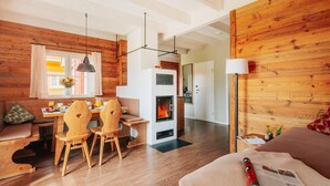 Una habitación acogedora con detalles de madera, un comedor con sillas y mesa de madera, una chimenea y una cama con una manta y una revista enrollada.