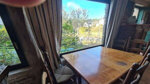 A dining area with a wooden table and chairs, large windows with a view of greenery and buildings. - Small house on the port (Bono)