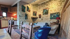 A cozy living room with a stone wall, wooden furniture, and colorful artwork. - Small house on the port (Bono)