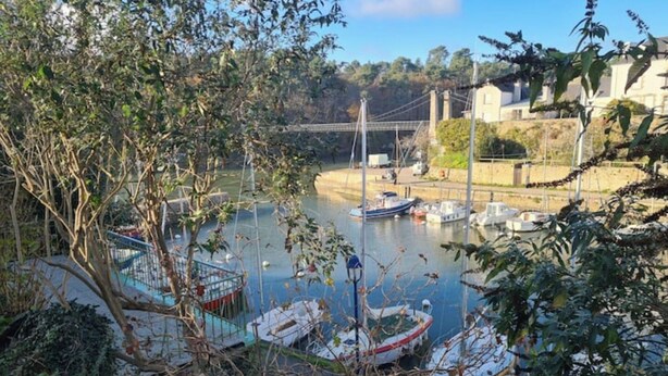 A river with boats docked, a bridge in the background, and greenery around. - Small house on the port (Bono)