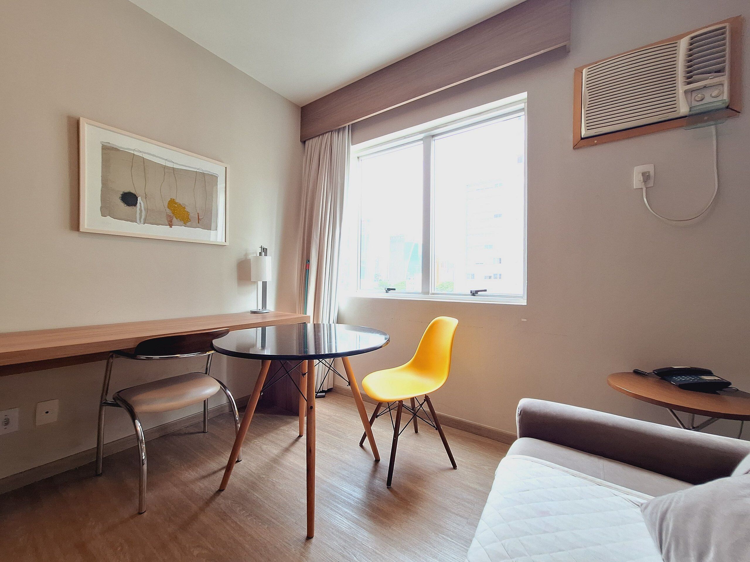 A hotel room with a bed, a desk, a chair, a small table, and a window with curtains.