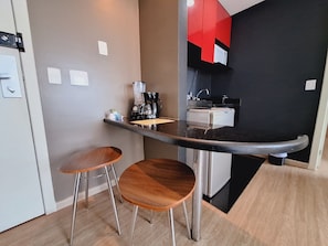 A compact kitchenette with a coffee maker, a small refrigerator, and two wooden stools. - Locking´s Barro Preto 2 (Belo Horizonte)
