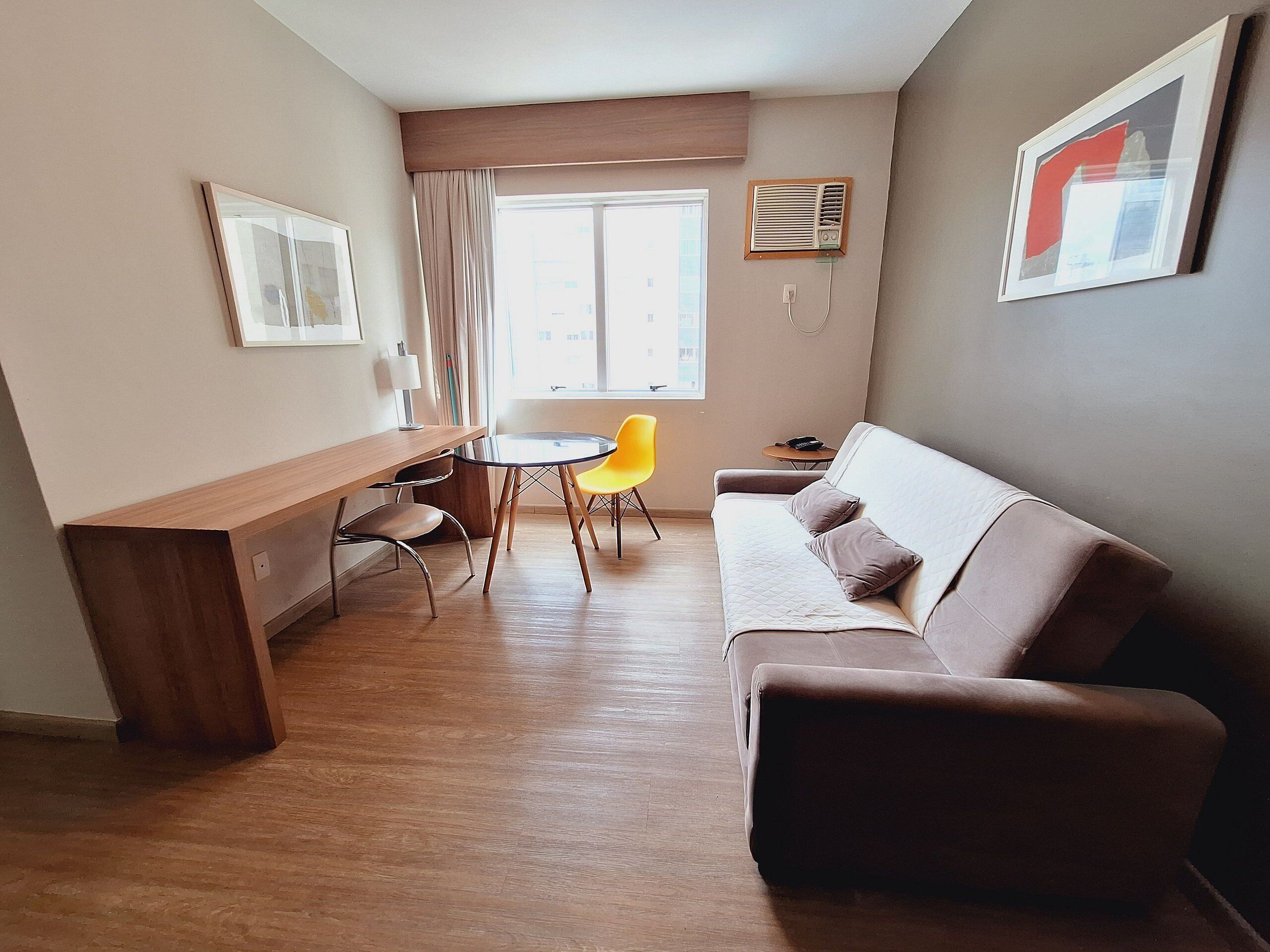 Un espacio habitable pequeño con un escritorio de madera, una silla amarilla, un sofá marrón y una mesita redonda.