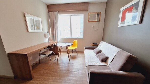 Un espacio habitable pequeño con un escritorio de madera, una silla amarilla, un sofá marrón y una mesita redonda.