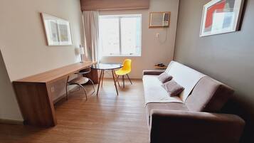 Un espacio habitable pequeño con un escritorio de madera, una silla amarilla, un sofá marrón y una mesita redonda.