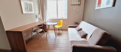 A compact living space with a wooden desk, a yellow chair, a brown sofa, and a small round table.