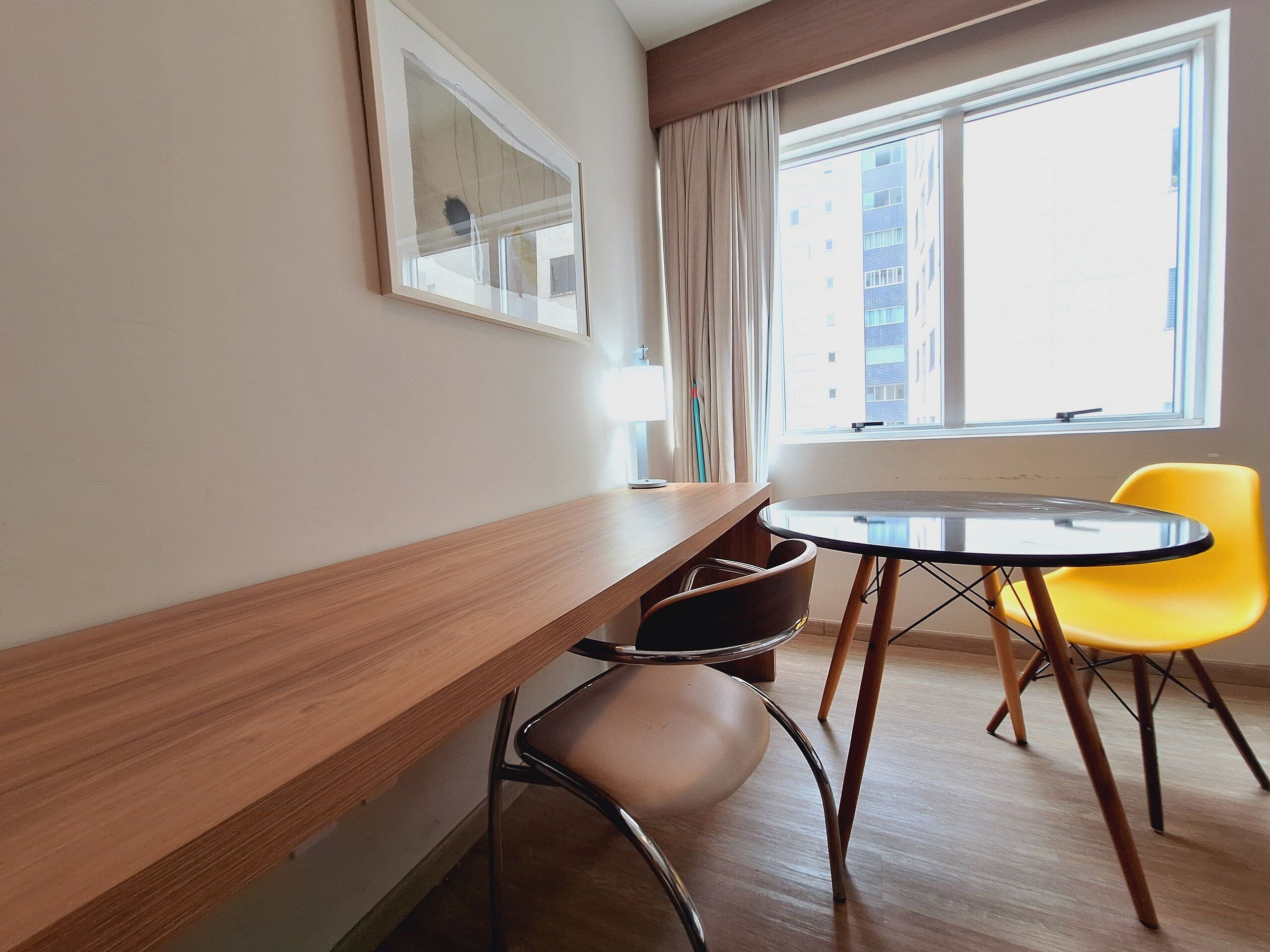 A modern room with a wooden desk, a round table, and two chairs, one yellow and one brown.