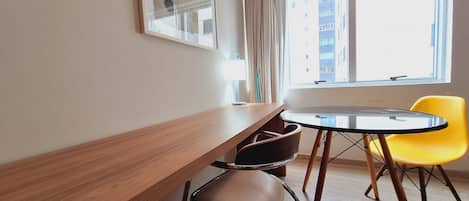 Una habitación moderna con un escritorio de madera, una mesa redonda y dos sillas, una amarilla y otra marrón.