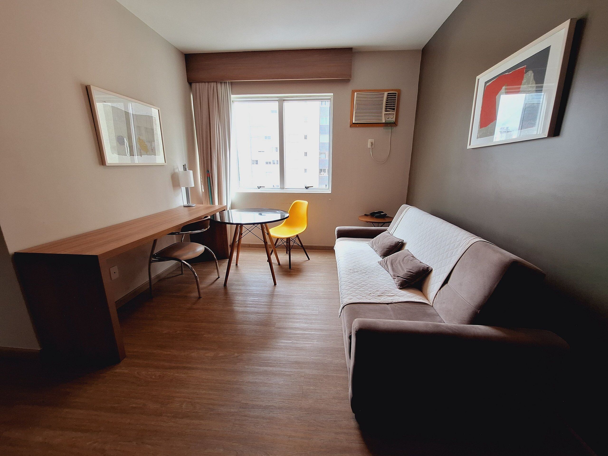 A modern living room with a brown sofa, a yellow chair, a wooden table, and a window with curtains.