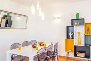 A dining area with a white table, black chairs, and a fruit bowl with oranges and apples.