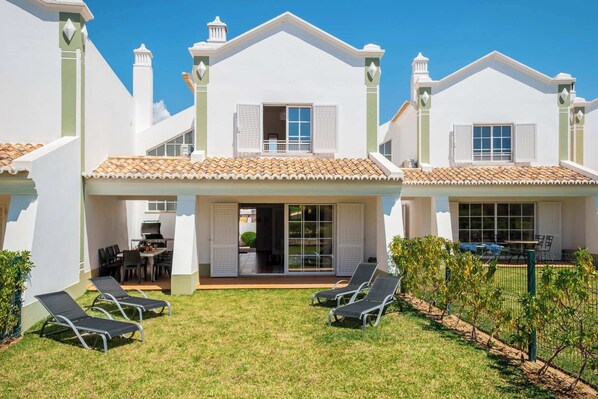 A two-story house with a patio, outdoor seating, and a small garden.