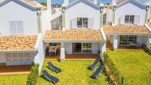 A row of white houses with tiled roofs and a grassy backyard with sun loungers.