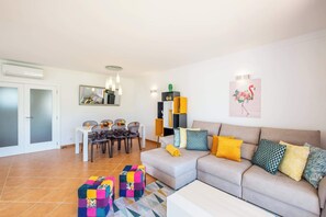 A modern living room with a sofa, colorful cushions, a dining table with chairs, and a small kitchen area. - Beachsun Gale - beautiful villa close to beach (Galé)