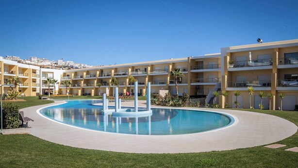 Un hotel moderno con una piscina central, varios balcones y vistas del entorno.