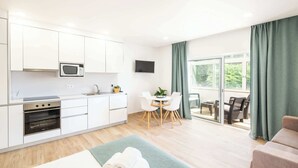 Eine moderne Küche mit weißen Schränken, einer Mikrowelle und einem Backofen. Es gibt eine Essecke mit Tisch und Stühlen, sowie ein Sofa.