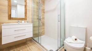 Ein modernes Badezimmer mit einer gläsernen Dusche, einem Holzausleger mit Spiegel und einer Toilette mit Handtuch darauf.