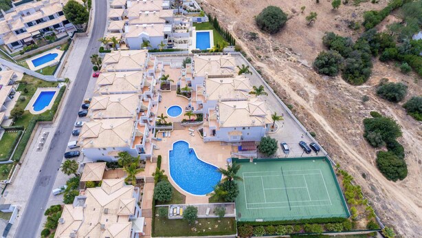 Vista aérea de un complejo residencial con varias casas, una piscina central y una cancha de tenis.