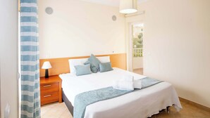 Un dormitorio con cama, mesita de noche, lámpara y vistas al exterior.