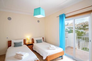 Two single beds with white linens and matching pillows, each with a wooden headboard and bedside table with a lamp.