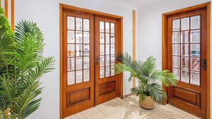 Een hal met houten dubbele deuren, potplanten en een betegelde vloer.