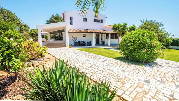Een modern herenhuis met twee verdiepingen, een overdekt terras, een geplaveid pad en weelderige begroeiing.
