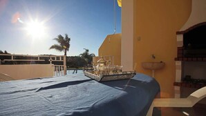 A sunlit room with a bed, a tray with glasses, and a view of palm trees and a building.