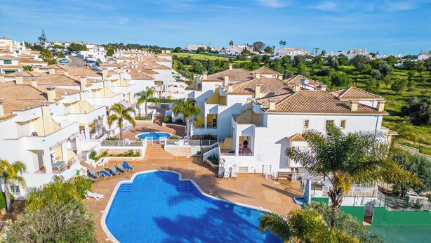 A resort with a swimming pool, white buildings, and a view of the surrounding area.