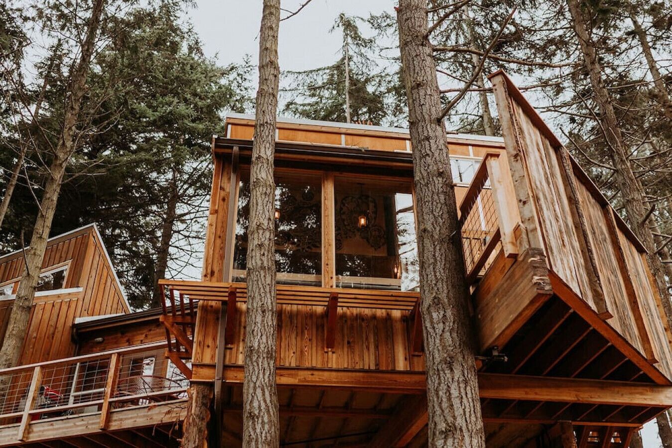 A wooden treehouse with a balcony, surrounded by tall trees.
