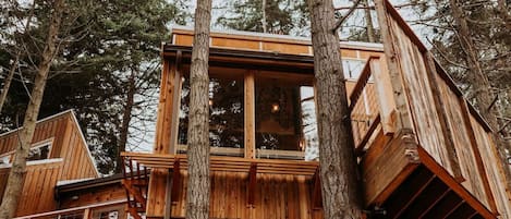 A wooden treehouse with a balcony, surrounded by tall trees.