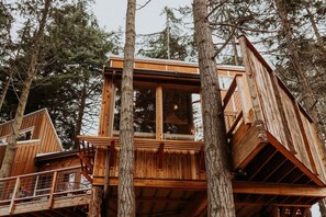 Una casa en el árbol de madera con balcón, rodeada de árboles altos.