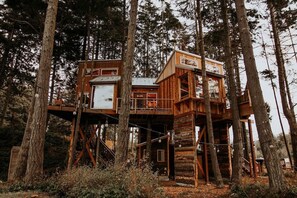 A treehouse cabin with multiple levels, wooden railings, and a rustic design.
