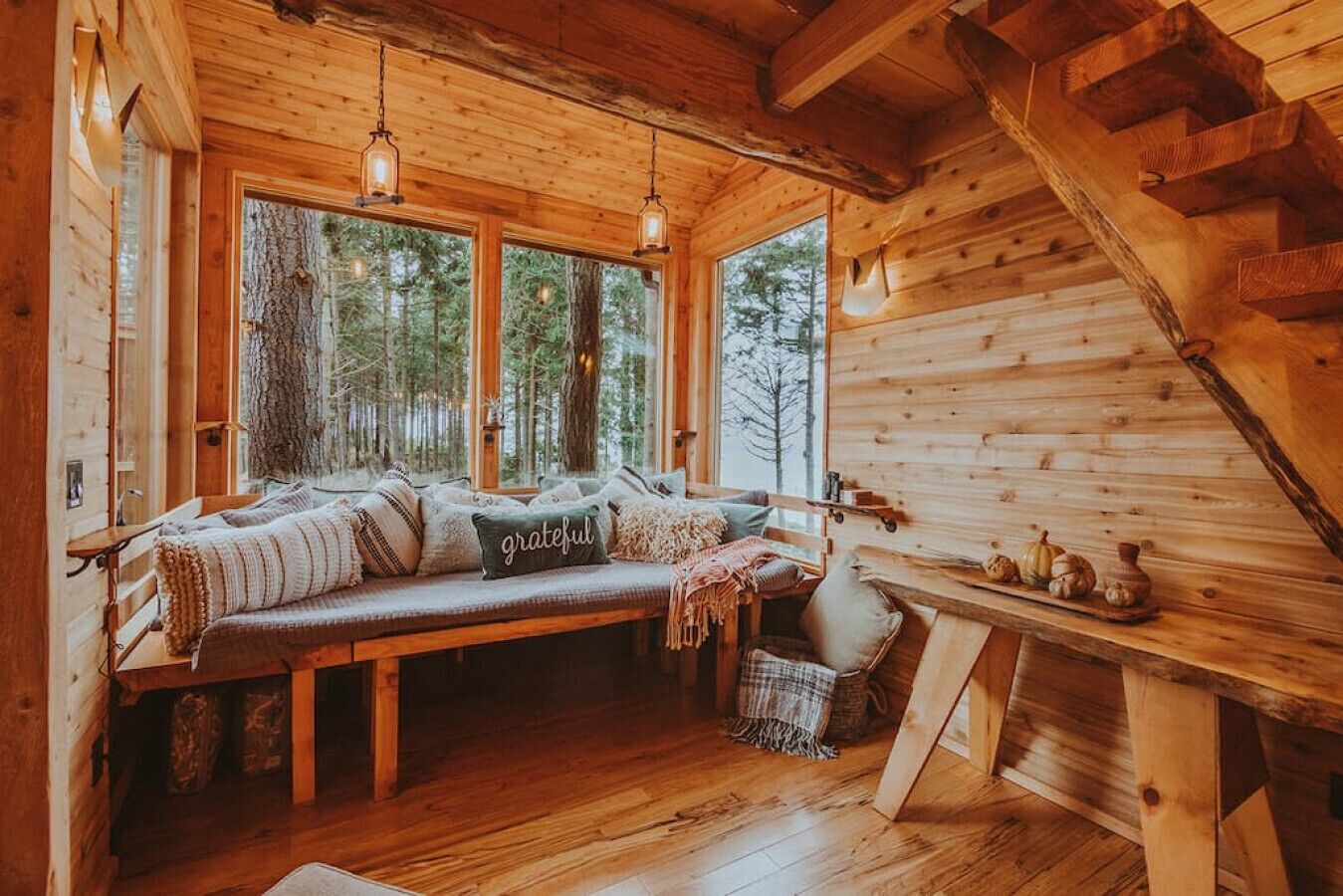 A cozy cabin interior with a wooden bench, large windows, and a staircase.