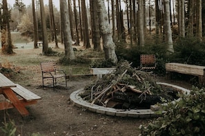 A rustic outdoor seating area with a wooden bench, a metal chair, and a fire pit surrounded by a stone border.